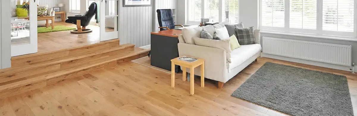 A modern living room with professionally installed laminate flooring, a beige sofa, a small side table, a gray rug, and large windows with white shutters in Memphis, TN
